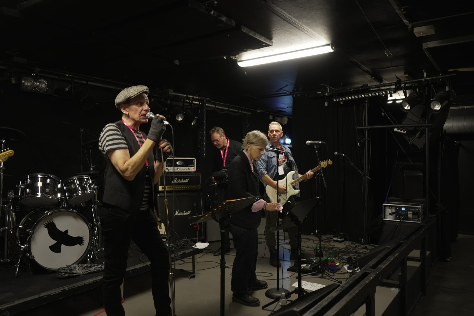 Rockband med sångare i keps på scen bland instrument och högtalare i mörkt scenljus