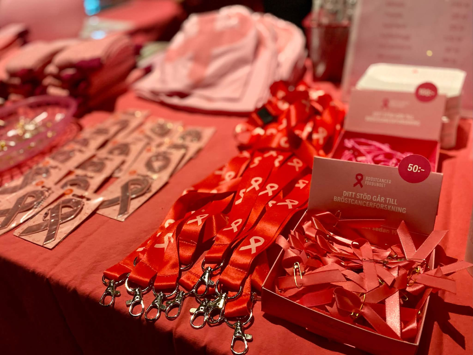 Bord med rosa bandet-merchandise: nyckelband, rosetter och pins med texten Bröstcancerförbundet