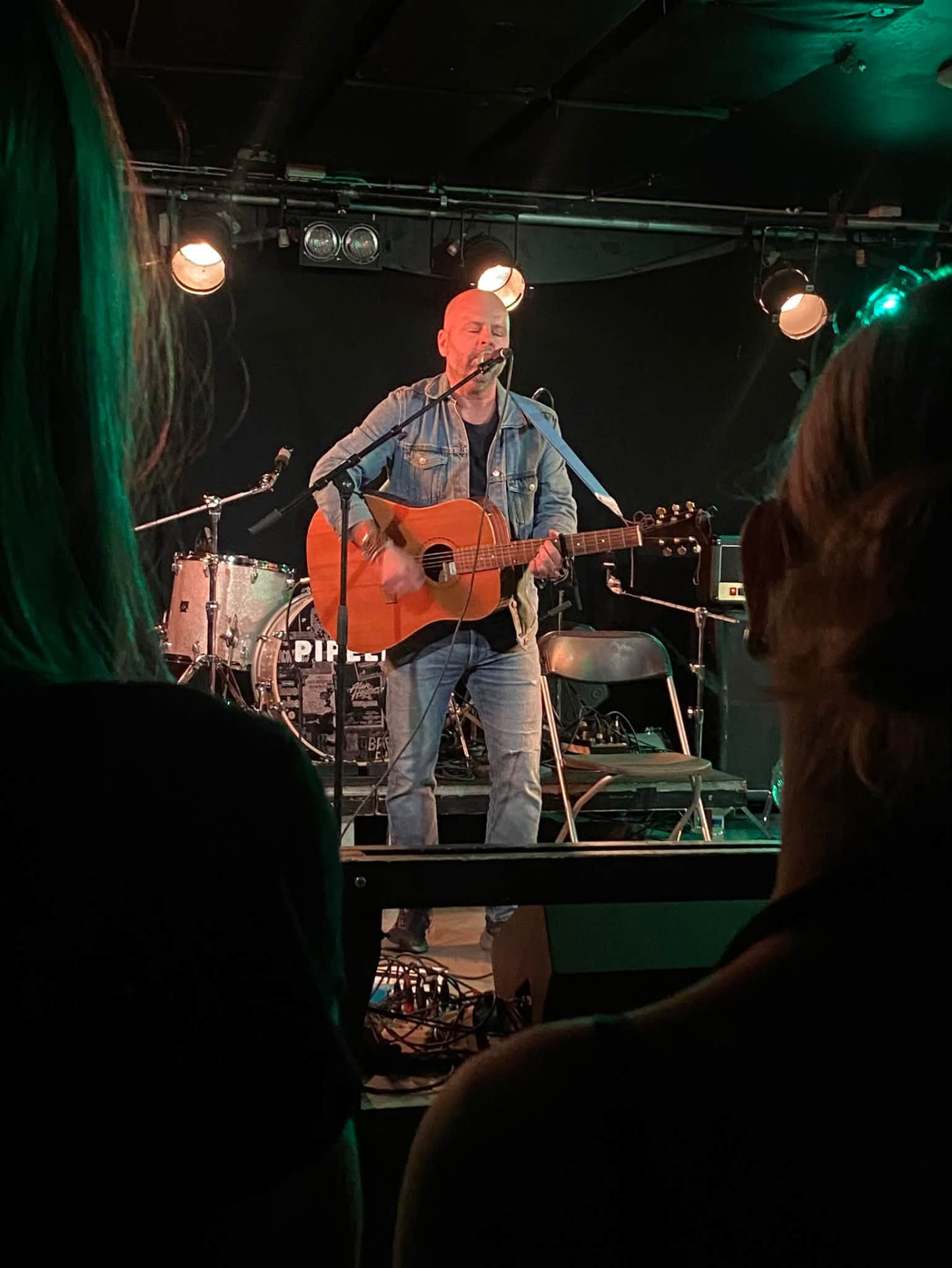 Artist som sjunger och spelar gitarr på scen sedd bakifrån, två personer i publiken i förgrunden